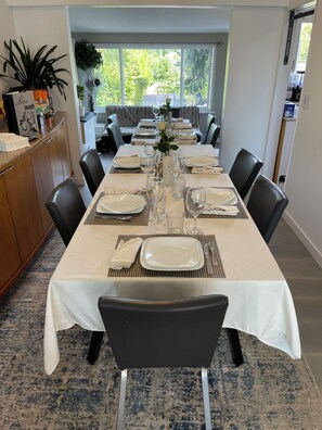 A dining area with a long table set for a meal, surrounded by chairs, with a view of greenery outside. - 5 Star 5 Bedroom Delta Home (Clean/Pet Friendly) Min 30 Days + 30% Discount (Delta)