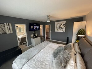 Ein Schlafzimmer mit einem Bett, einem Fernseher, Kunstwerken an den Wänden und einem Deckenventilator.