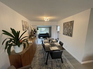 Ein moderner Essbereich mit einem langen Tisch für vier Personen, einer Küchenzeile mit Topfpflanze und Blick zum Esszimmer.