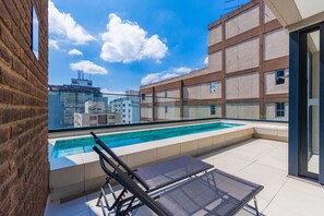 A rooftop pool area with a glass balustrade, a lounge chair, and a view of the cityscape. - Studio c Piscina e Academia a 400m da Av Paulista (São Paulo)