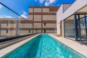 Une piscine à l’eau d’un bleu cristallin, entourée d’un bâtiment moderne doté de grandes fenêtres et d’une balustrade en verre.