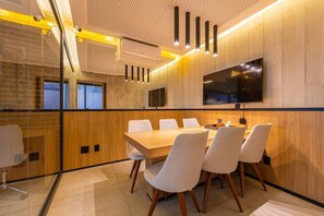 A conference room with a long table, six chairs, a flat-screen TV, and a wooden accent wall. - Studio c Piscina e Academia a 400m da Av Paulista (São Paulo)