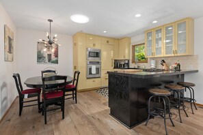 A modern kitchen with a central island, bar stools, and a dining area with chairs. - Escape to Casita at East Beach! (Santa Barbara)