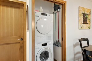 A compact laundry room with a front-loading washing machine, a dryer, and a mop. - Escape to Casita at East Beach! (Santa Barbara)