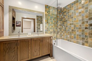 Ein Badezimmer mit einem Holzbadezimmermöbel, einem großen Spiegel, einer Badewanne und einer Dusche mit Mosaikfliesen.