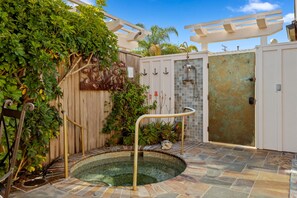 Ein privater Bereich mit Whirlpool im Freien, einer Holzpergola, einem gefliesten Pool und einem Metalltor.