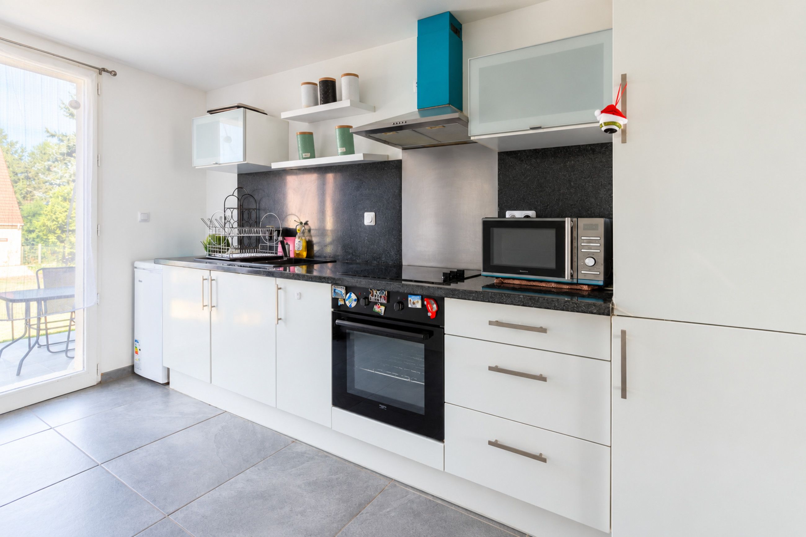 A modern kitchen with white cabinets, a black countertop, and a built-in oven.