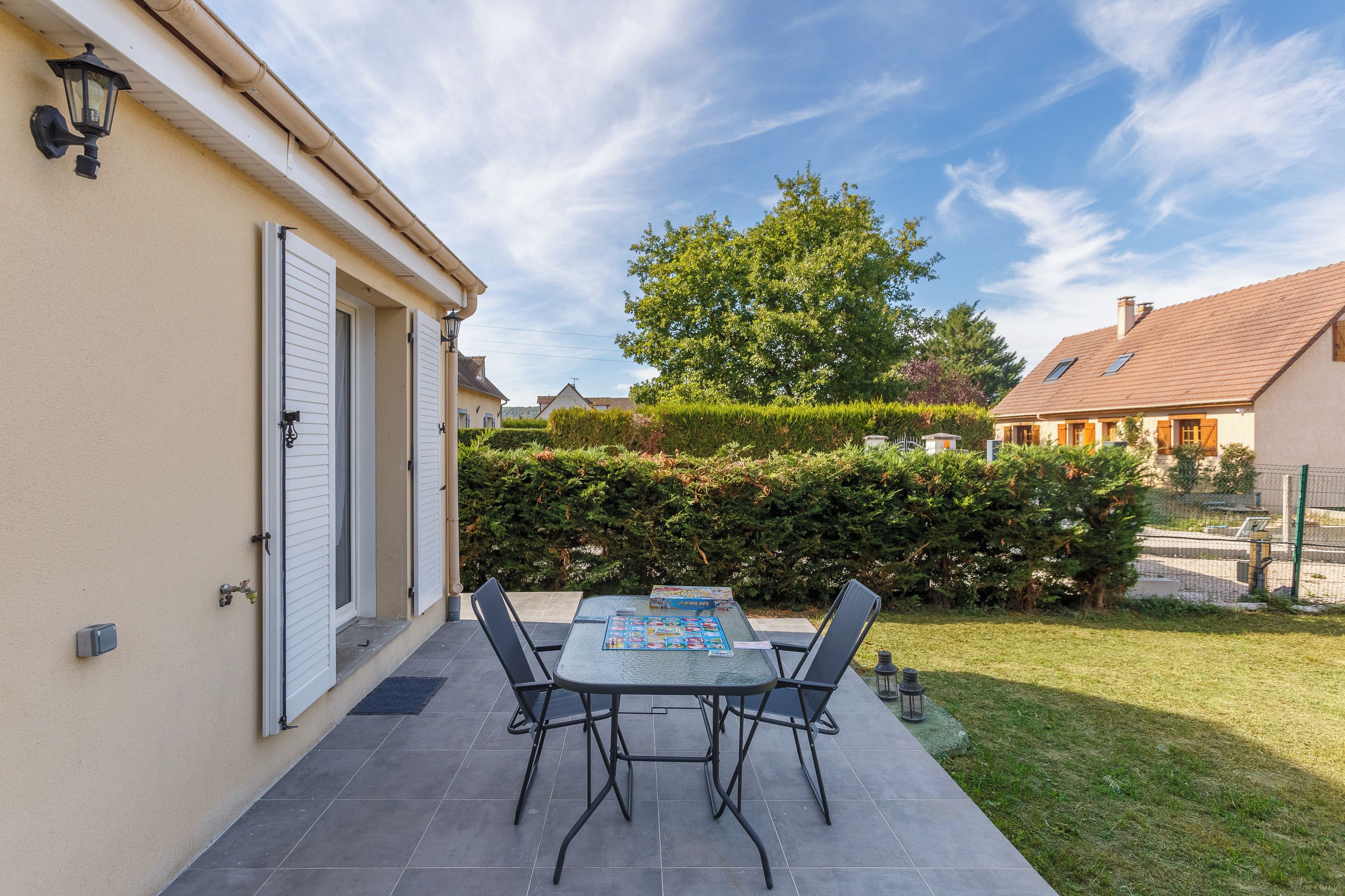A patio with a table and chairs, a small garden, and a building with a door and windows.