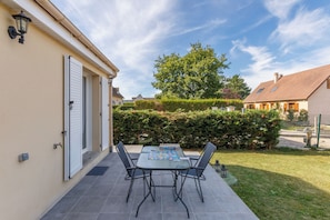 Eine Terrasse mit Tisch und Stühlen, ein kleiner Garten und ein Gebäude mit Tür und Fenstern.