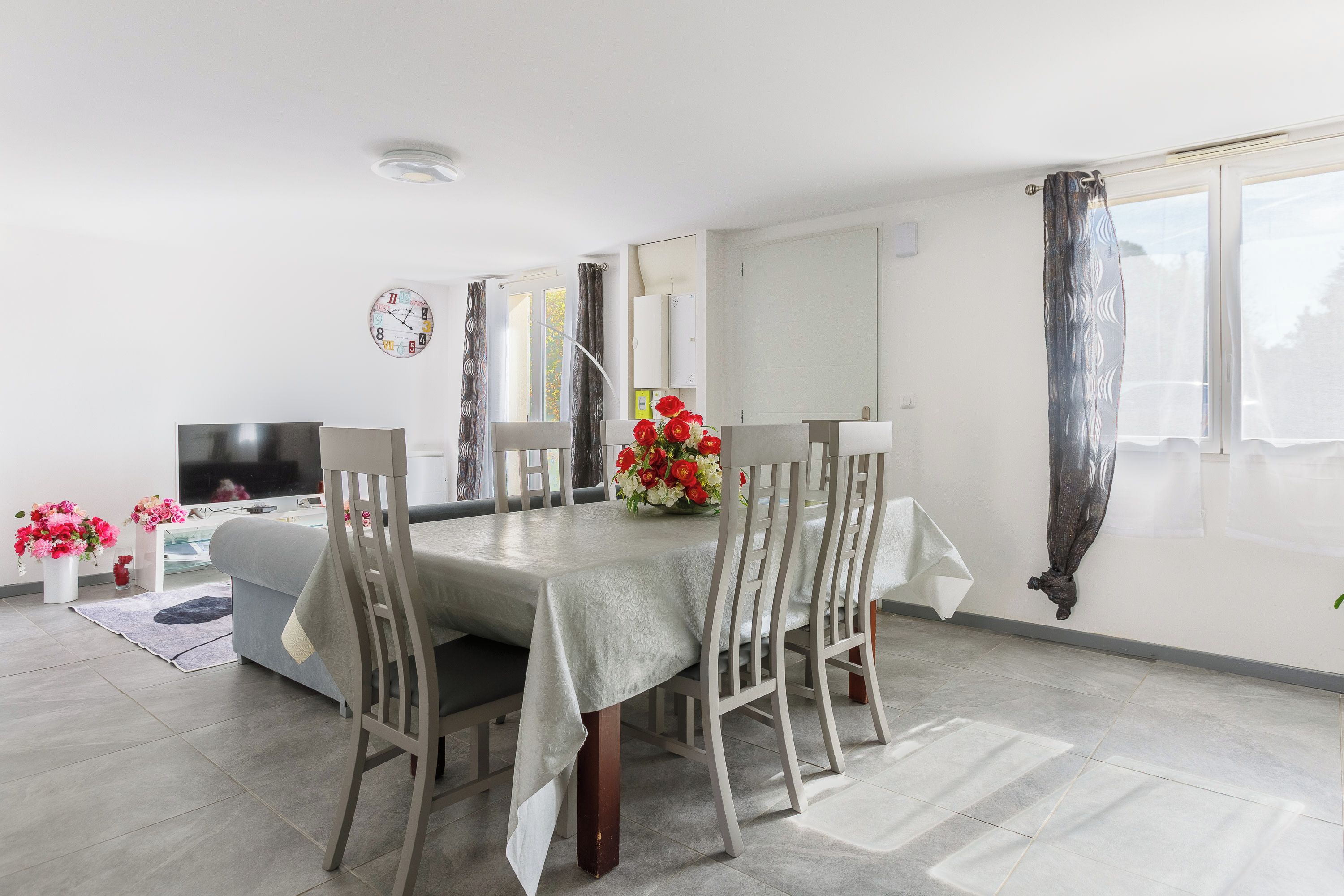 A dining area with a table, chairs, a TV, and a clock on the wall.