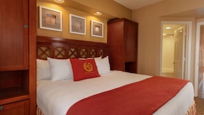 Una habitació d'hotel amb un llit gran, un capçal de llit de fusta i una manta vermella. Hi ha tres quadres emmarcats a la paret sobre el llit.