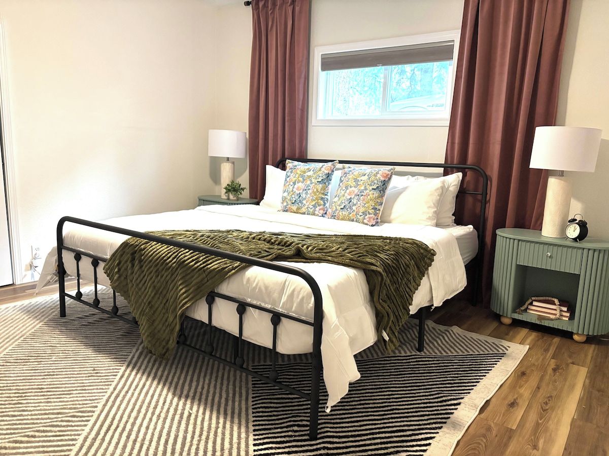 A neatly arranged bedroom with a bed, bedside lamps, a nightstand, and a window with curtains.