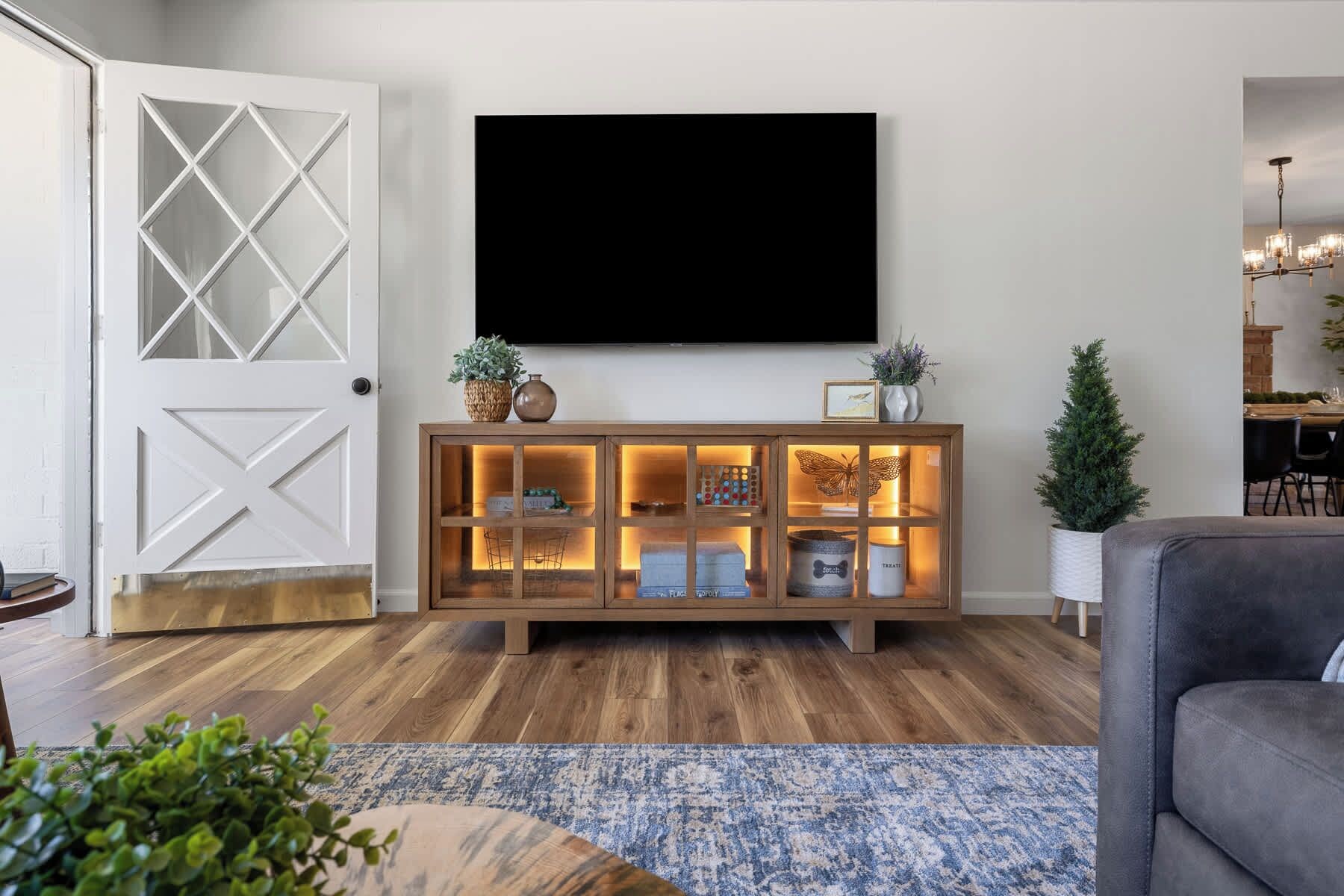 Un salon comprenant une console en bois, un téléviseur à écran plat fixé au mur et un coin repas avec une table et des chaises.
