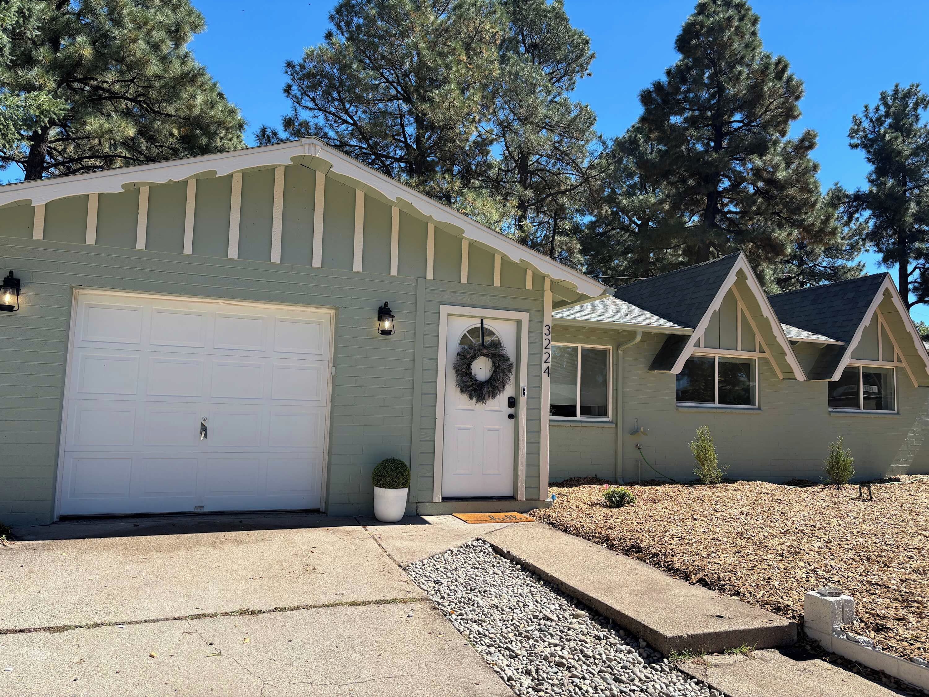 A single-story house with a garage, a front door with a wreath, and a small front yard with gravel and plants.