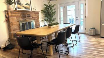A dining area with a long wooden table, black chairs, a brick fireplace, and a large potted plant.