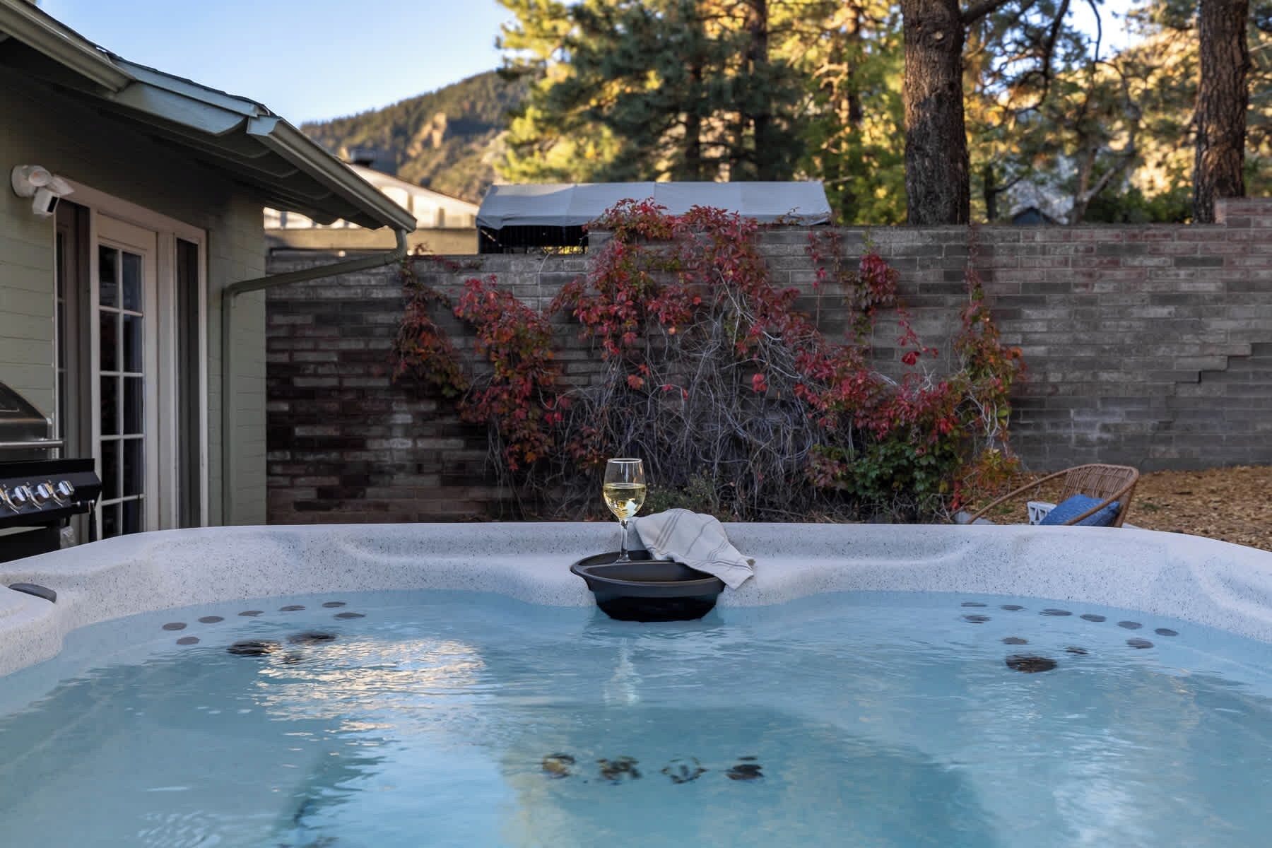 A hot tub with a glass of white wine, surrounded by a brick wall and a wooden deck.