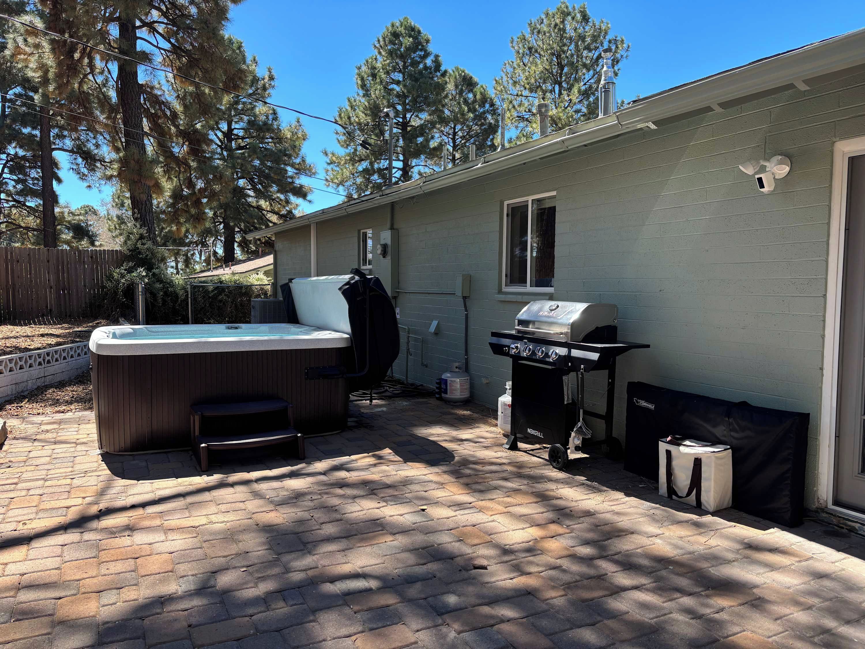A backyard with a hot tub, a grill, and a brick patio.