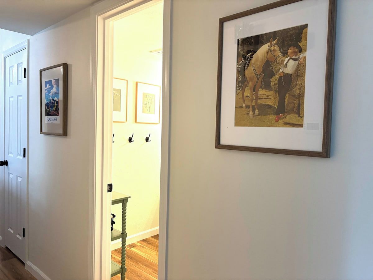 A hallway with framed pictures on the walls, a door on the left, and a staircase leading to an upper level.