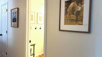 A hallway with framed pictures on the walls, a door on the left, and a staircase leading to an upper level.