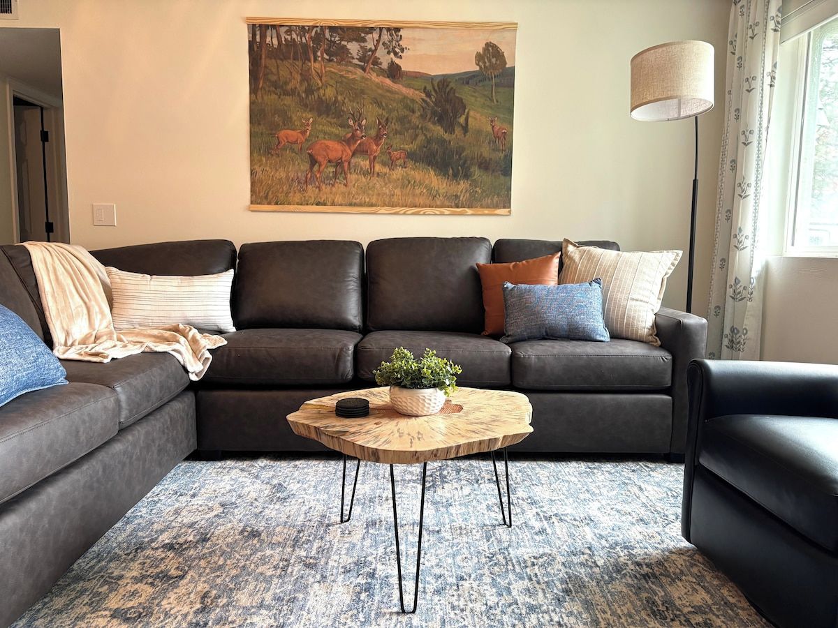 A living room with a sectional sofa, a round coffee table with a plant, and a painting on the wall.