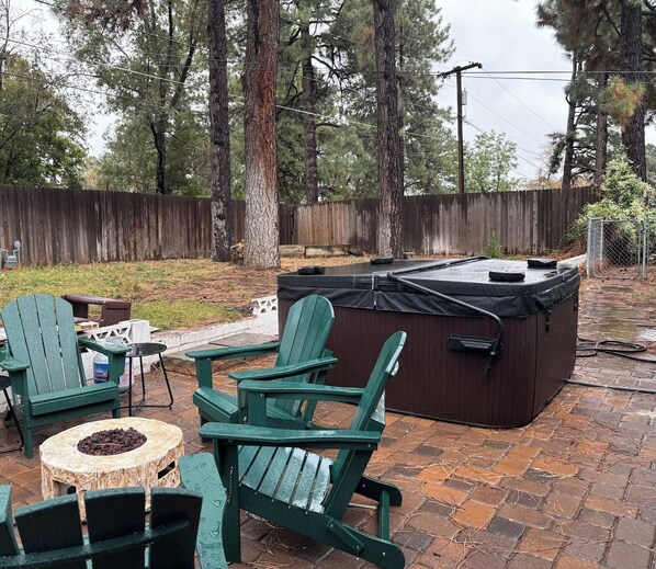 Un patio al aire libre con sillas Adirondack verdes, un jacuzzi y un pozo de fuego de piedra.