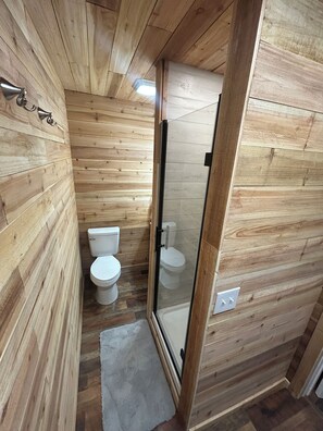 Un baño con paneles de madera, cabina de ducha de vidrio y un inodoro blanco.