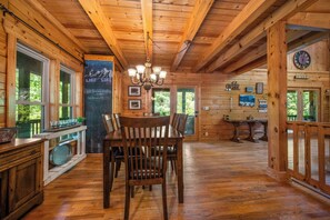 A wooden cabin interior with a dining table, chairs, a chandelier, and a large window. - Lake Lure Lakefront Home with Private Par 3 (Lake Lure)
