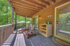 A wooden deck with two Adirondack chairs and a small table, overlooking a lush green landscape. - Lake Lure Lakefront Home with Private Par 3 (Lake Lure)