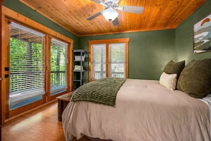 A bedroom with a bed, a ceiling fan, and a view of greenery through the windows. - Lake Lure Lakefront Home with Private Par 3 (Lake Lure)