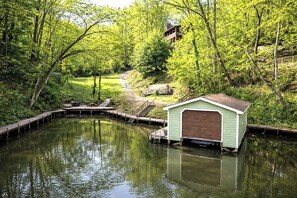 A tranquil riverside scene with a small shed and a dock extending into the water. - Lake Lure Lakefront Home with Private Par 3 (Lake Lure)