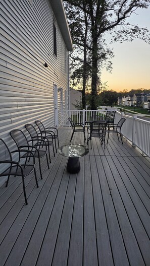 A wooden deck with metal chairs and a glass table, surrounded by a white railing. - Crandall Luxe Retreat (Lanham)