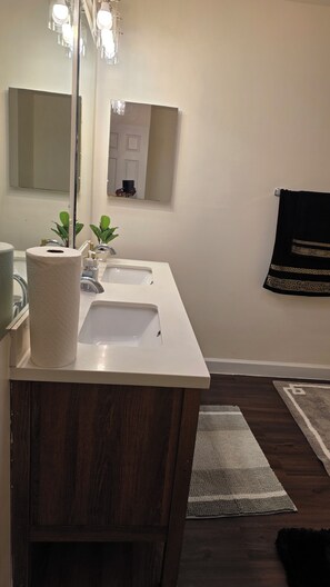 A bathroom with a white vanity, two sinks, a mirror, and a towel rack. - Crandall Luxe Retreat (Lanham)