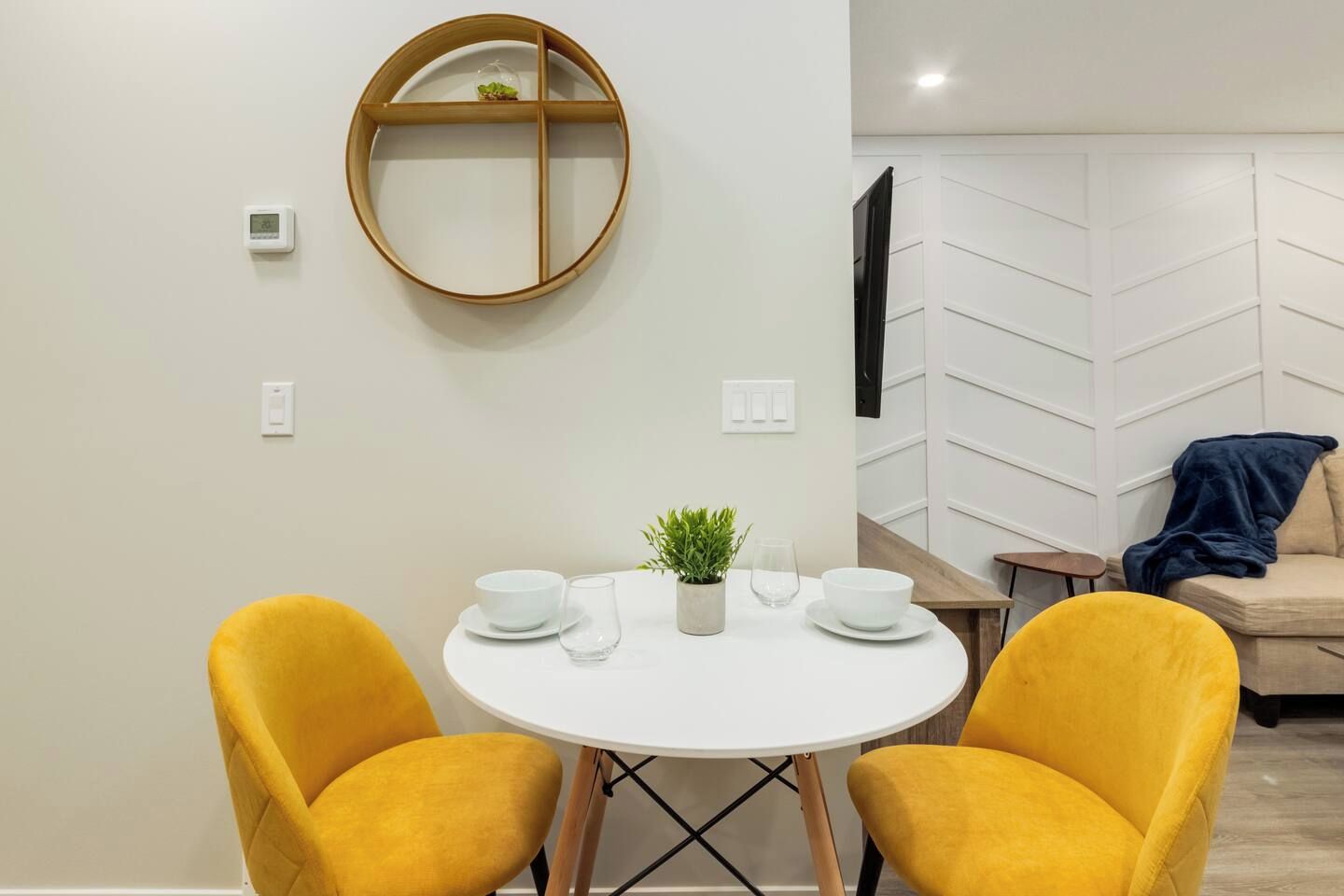 A modern dining area with a round table, two yellow chairs, a small potted plant, and white bowls and glasses.