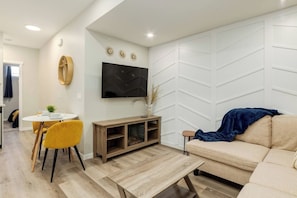 Ein modernes Wohnzimmer mit einer Couch, einem an der Wand montierten Fernseher, einem Essbereich mit Tisch und Stühlen sowie einer Holz-Multimöbel-Anlage.