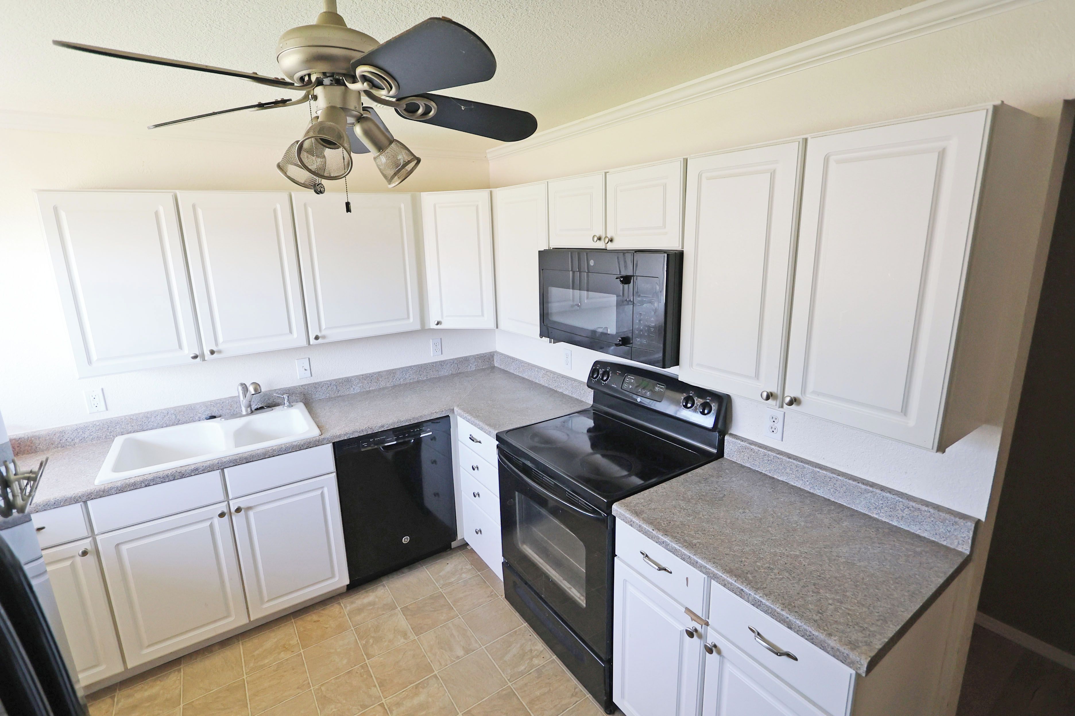 A kitchen with white cabinets, a black stove, a dishwasher, and a ceiling fan.