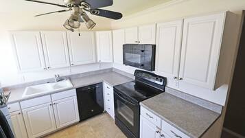 A kitchen with white cabinets, a black stove, a dishwasher, and a ceiling fan.