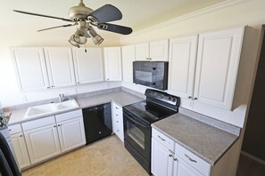 A kitchen with white cabinets, a black stove, a dishwasher, and a ceiling fan.