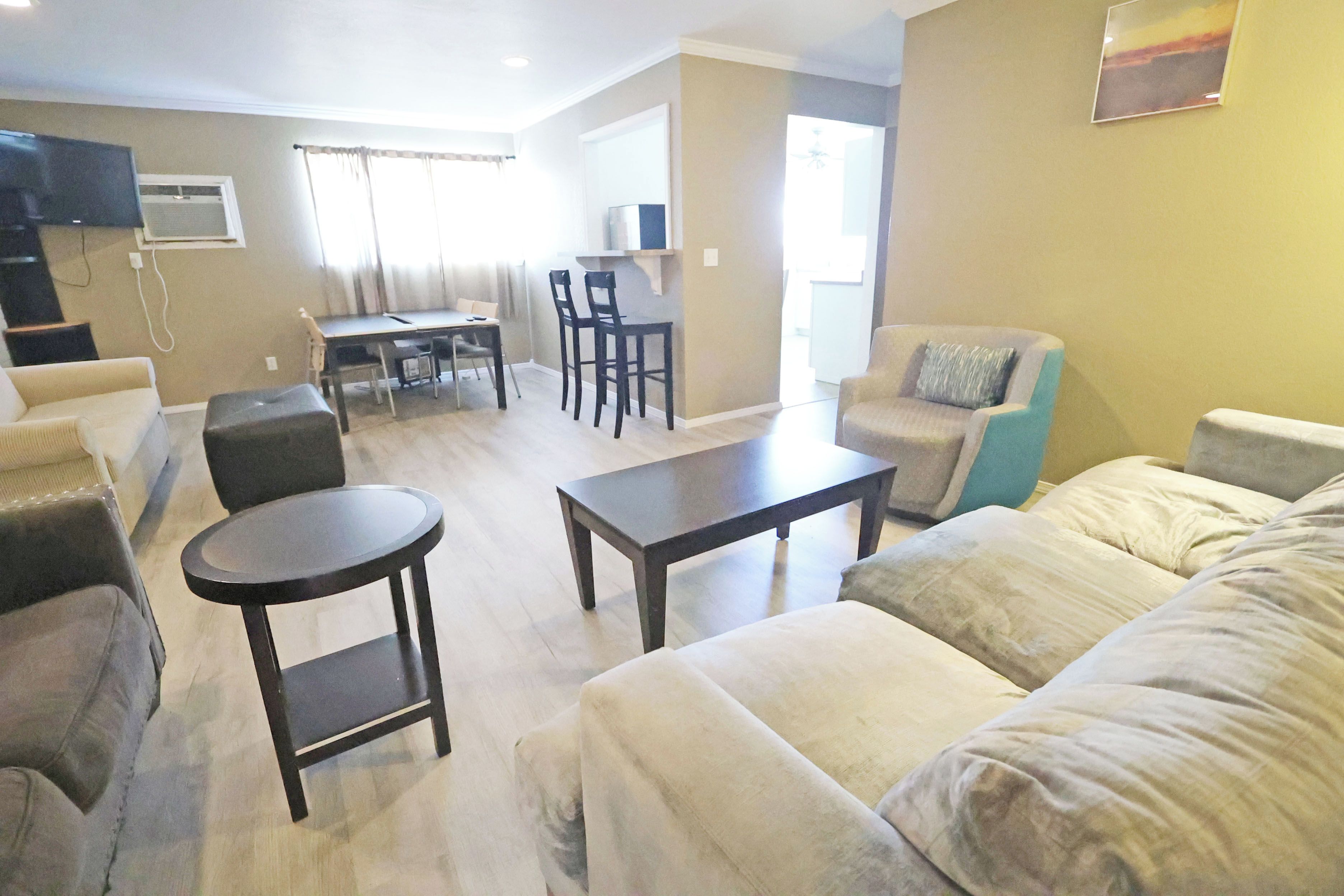A living room with a sofa, a coffee table, and a TV. There is a dining area with chairs and a table.