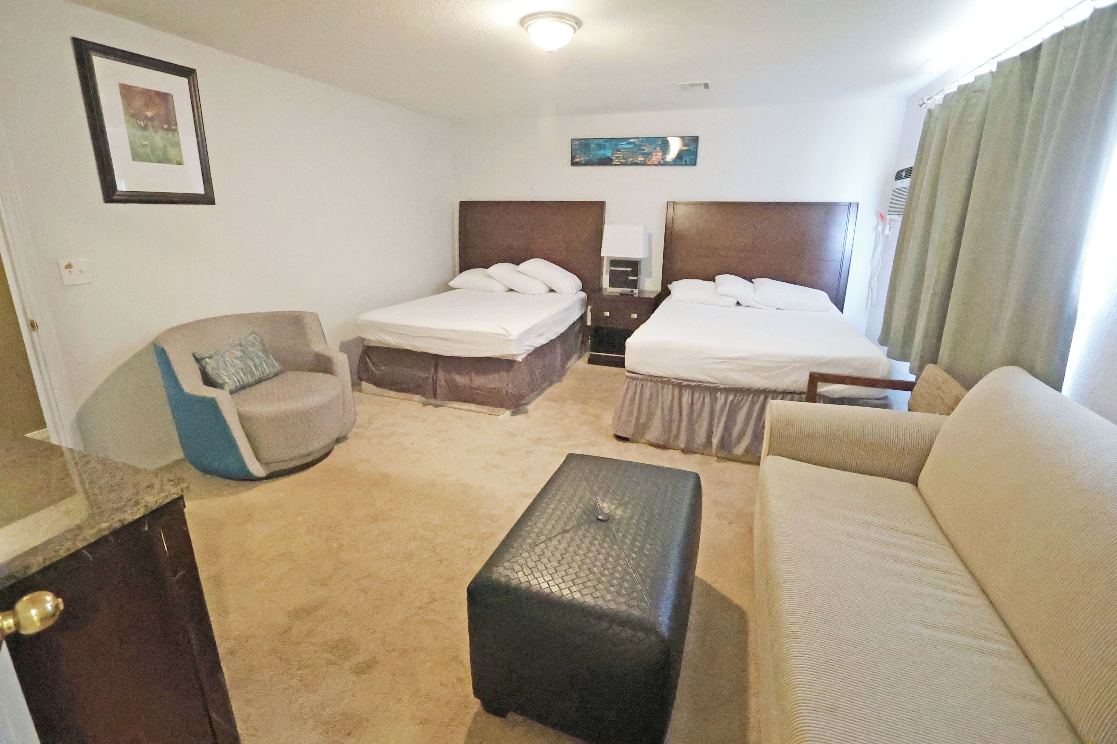 Ett hotellrum med två sängar, en soffa, en fåtölj, ett litet bord och en tavla på väggen.
