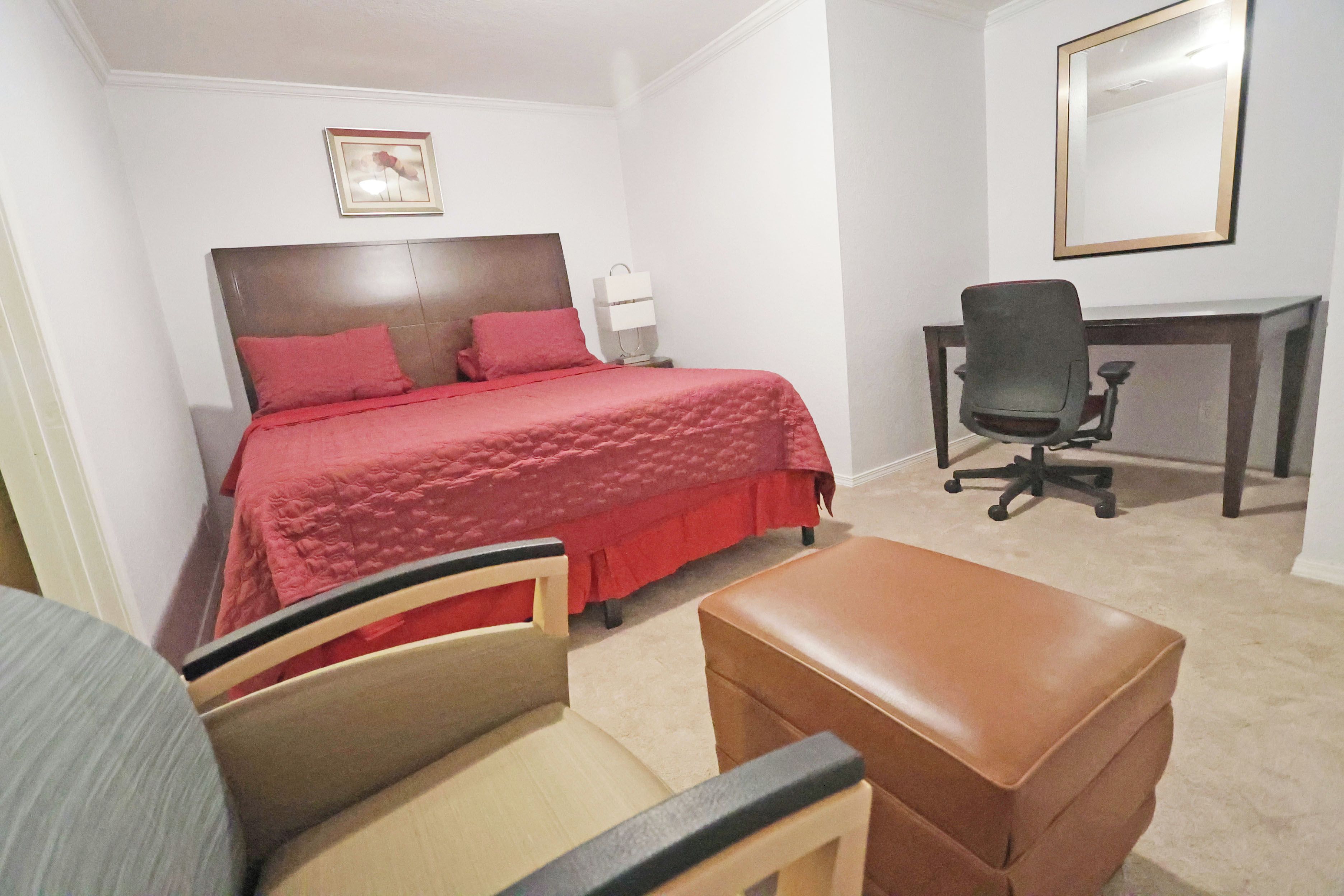 A bedroom with a bed, a desk, a chair, and a small table.