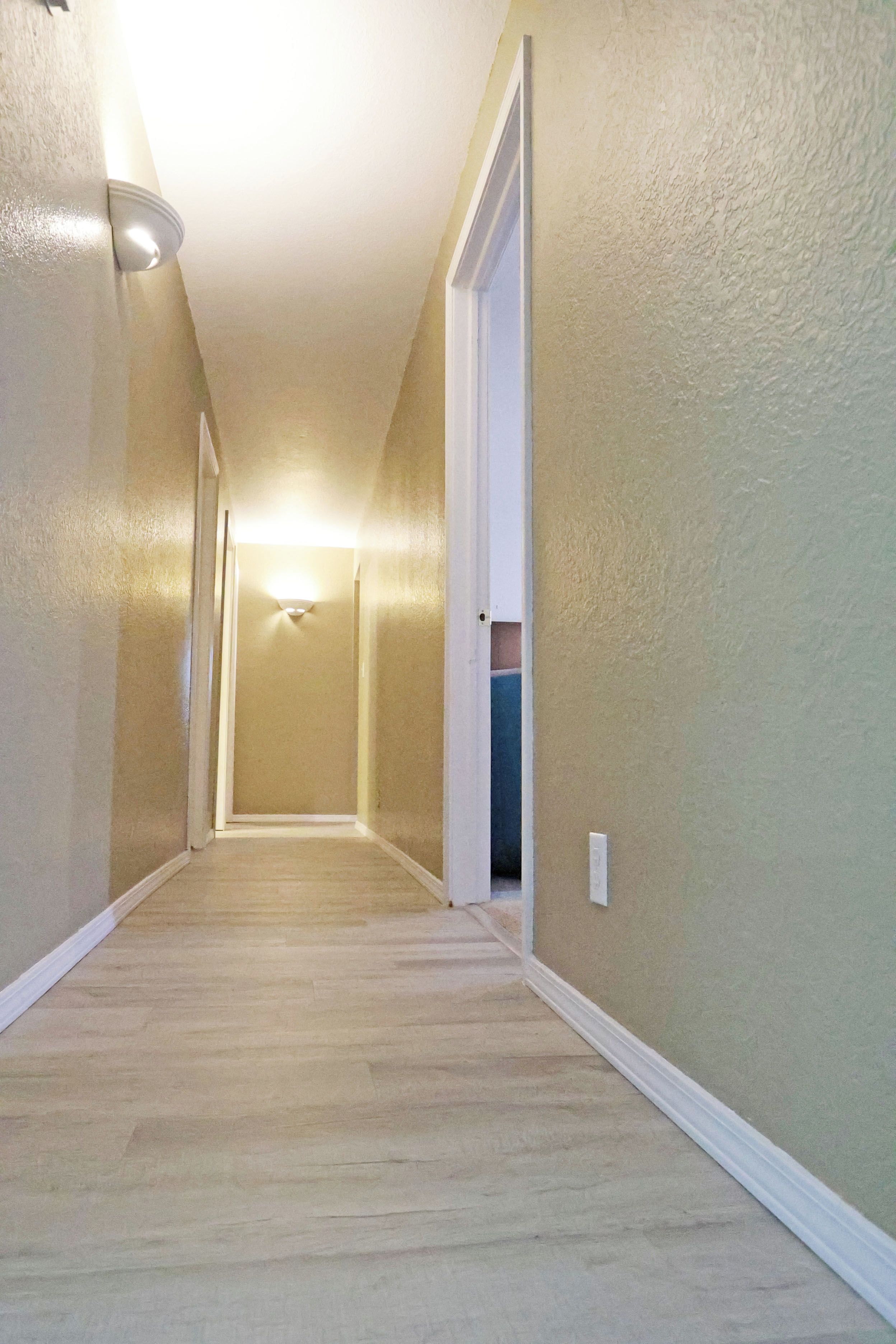 A hallway with a carpeted floor, white trim, and a light fixture on the ceiling.