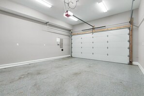 A clean, empty garage with a large garage door, fluorescent lighting, and a ceiling-mounted projector. - Home with Rooftop Patio + Garage, by 12 South and 2 miles to Broadway (Nashville)