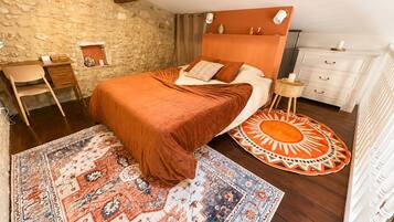 Une chambre avec un mur en pierre, un cadre de lit en bois, un tapis à motifs et une commode blanche.