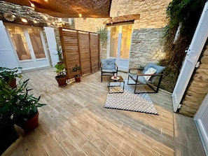 A cozy patio area with stone walls, wooden furniture, and potted plants.