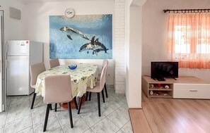 Ein Essbereich mit Tisch, Stühlen, einem Bild von Delfinen, einem Fernseher und einer Küchenzeile mit Kühlschrank.