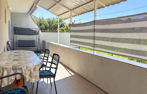 Ein Balkon mit Tisch und Stühlen, ein überdachter Bereich und Blick ins Grüne.