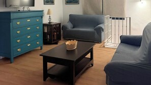 A living room with a blue sofa, a matching armchair, a coffee table with a decorative bowl, a blue dresser with gold handles, and a television mounted on the wall. - Hacienda El Descanso El Bosque by Ruralidays (Cádiz)
