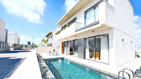 A modern two-story building with a swimming pool, large windows, and a staircase leading to the upper floor.