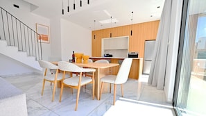 A modern kitchen with wooden cabinets, a dining area with a table and chairs, and a staircase with a railing.