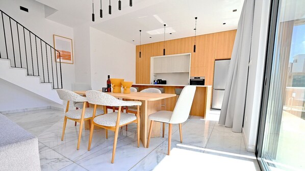 Una cocina moderna con armarios de madera, un comedor con mesa y sillas, y una escalera con barandilla.